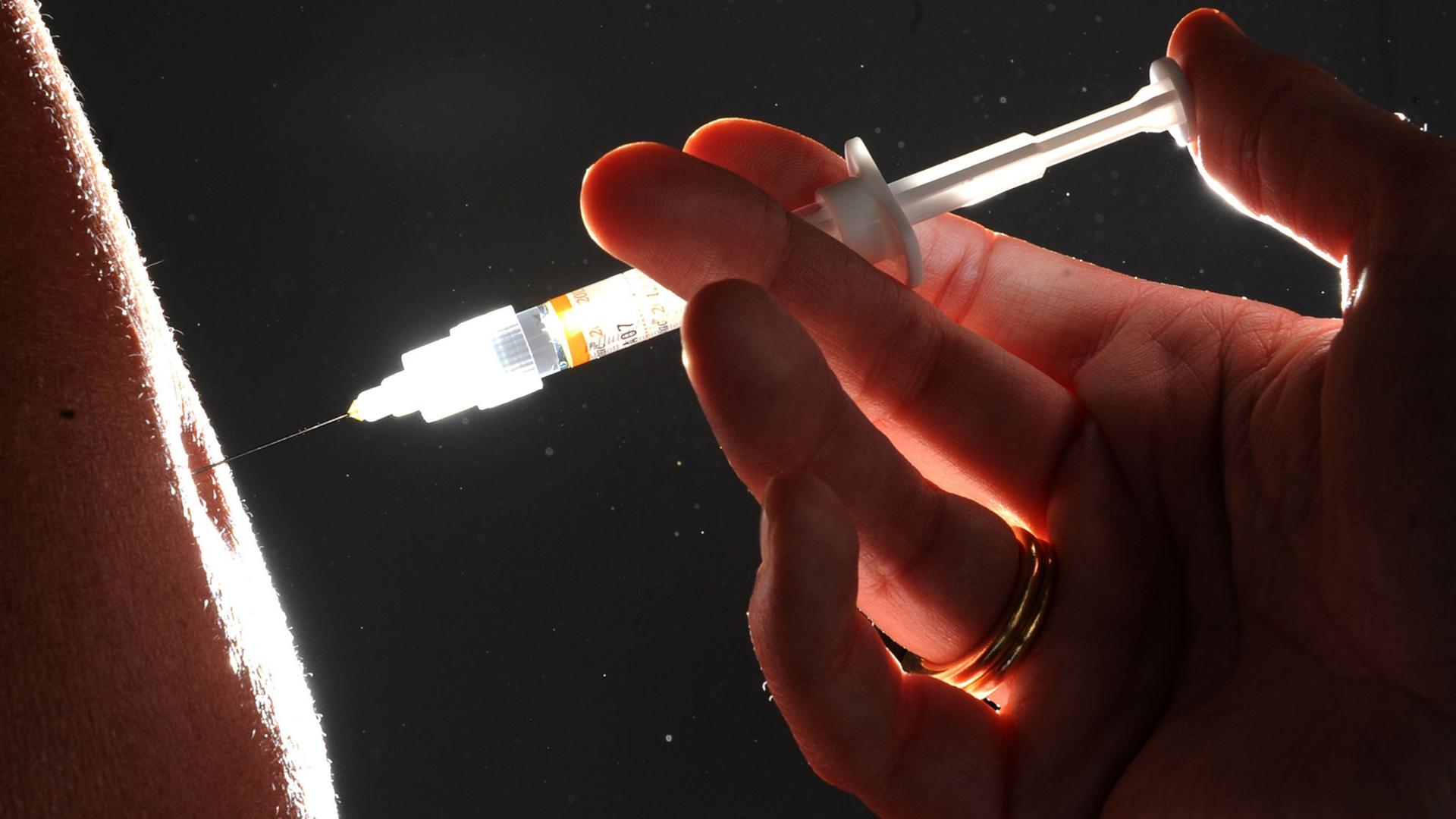Eine Spritze sticht in einen Arm Eine Spritze sticht in einen Arm