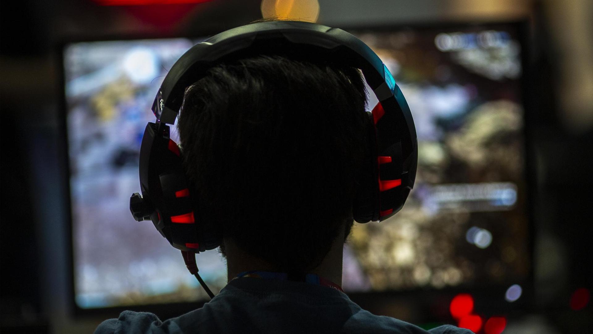 Ein Gamer mit Kopfhörern von hinten vor dem Bildschirm im Convention Center in Los Angeles. Ein Gamer mit Kopfhörern von hinten vor dem Bildschirm im Convention Center in Los Angeles.