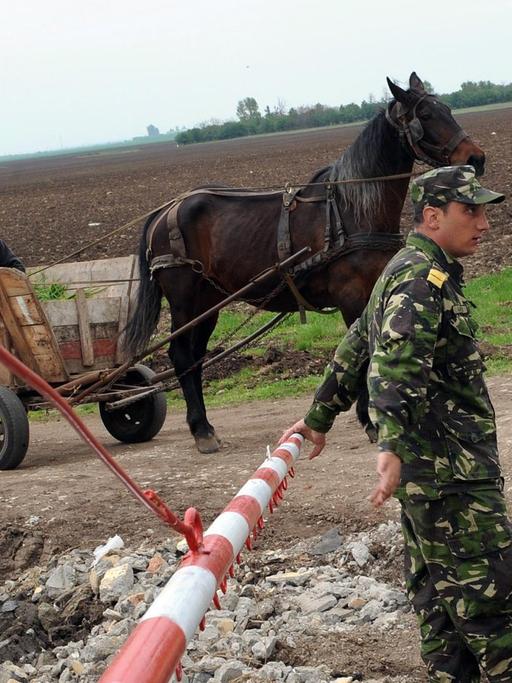 Ein rumänischer Soldat an einer Barriere nahe des militärischen Stützpunktes. Im Hintergrund ein Einwohner des Dorfes auf einem Pferdekarren.