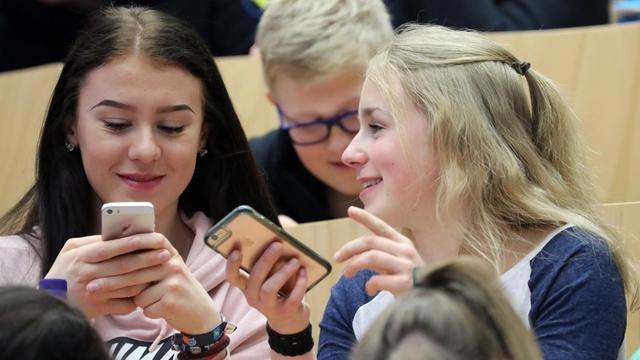 Drei Mädchen haben ihr Smartphone in der Hand und sprechen miteinander