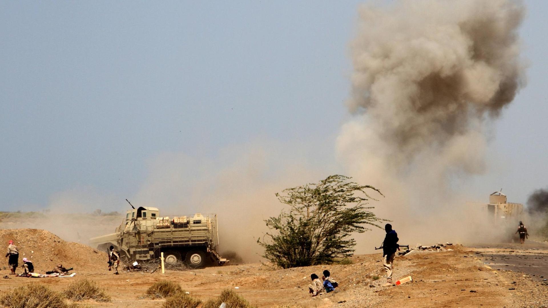 Eine Landmine im Jemen explodiert, eine Rauchwolke steigt auf, im Vordergrund ducken sich Menschen.