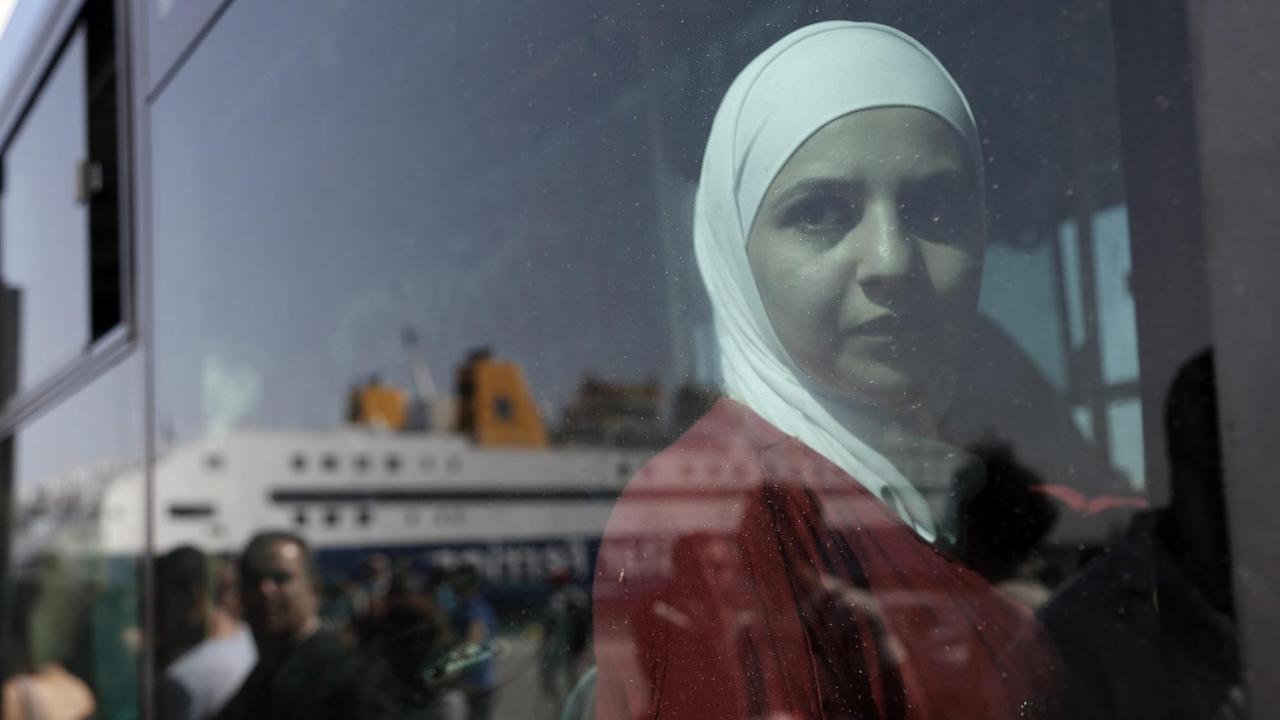 Eine syrische Frau schaut aus dem Fenster eines Reisebus', in dessen Fenster sich die Fähre "Diagoras" reflektiert, die gerade im Hafen von Piraeus, nahe Athen, ankommt. Eine syrische Frau schaut aus dem Fenster eines Reisebus', in dessen Fenster sich die Fähre "Diagoras" reflektiert, die gerade im Hafen von Piraeus, nahe Athen, ankommt.