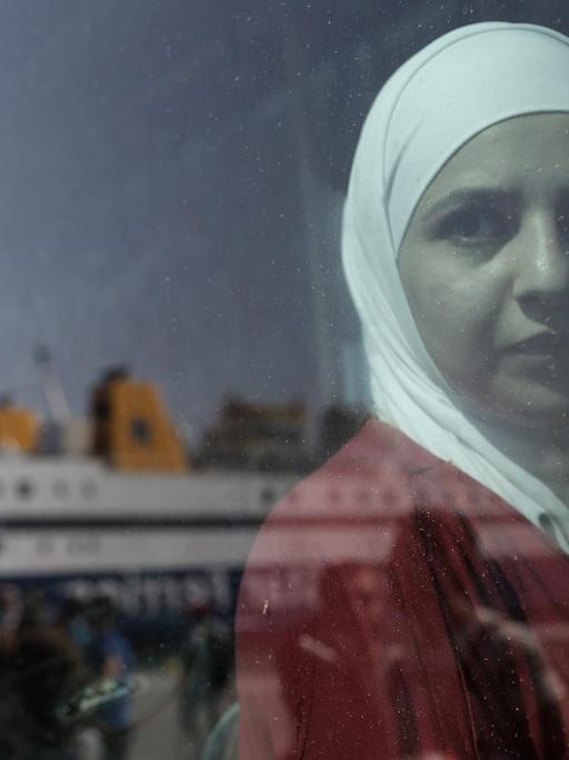 Eine syrische Frau schaut aus dem Fenster eines Reisebus', in dessen Fenster sich die Fähre "Diagoras" reflektiert, die gerade im Hafen von Piraeus, nahe Athen, ankommt.