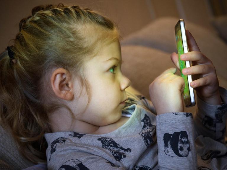  Ein kleines Mädchen spielt auf einem Smartphone.