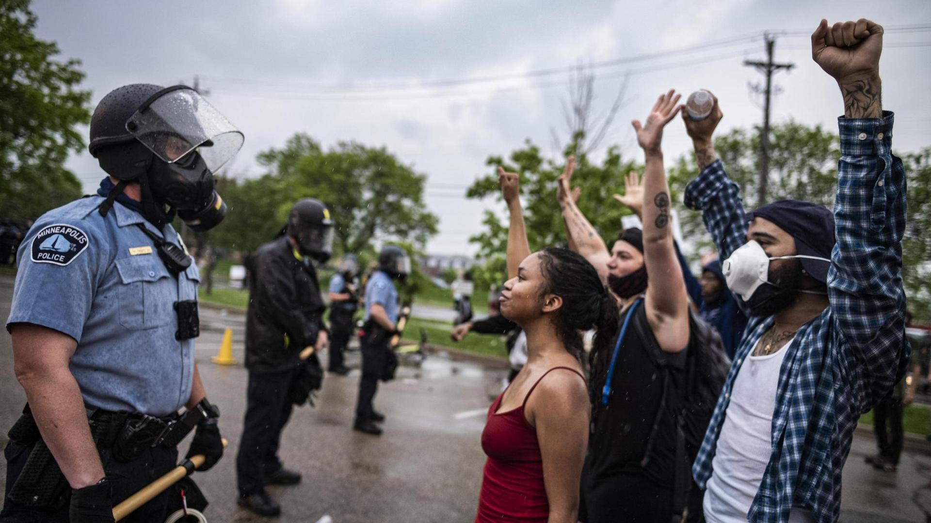 Mehrere Demonstranten mit Atemschutzmasken stellen sich protestierend vor eine Reihe von Polizisten. Mehrere Demonstranten mit Atemschutzmasken stellen sich protestierend vor eine Reihe von Polizisten.