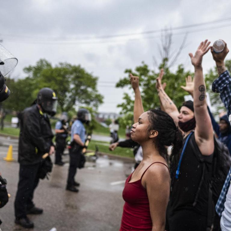 Mehrere Demonstranten mit Atemschutzmasken stellen sich protestierend vor eine Reihe von Polizisten.