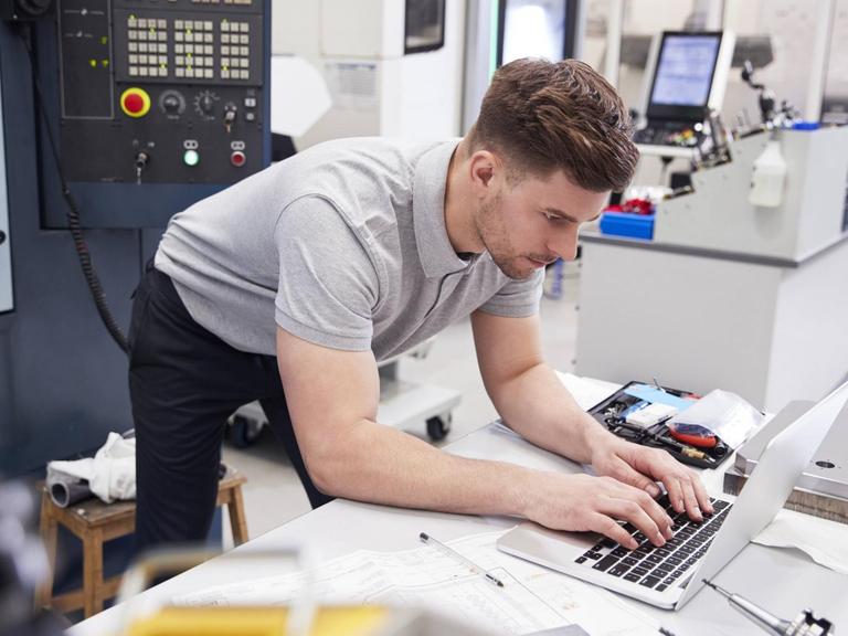 Ein junger Mann steht am Laptop in einem Technologizentrum