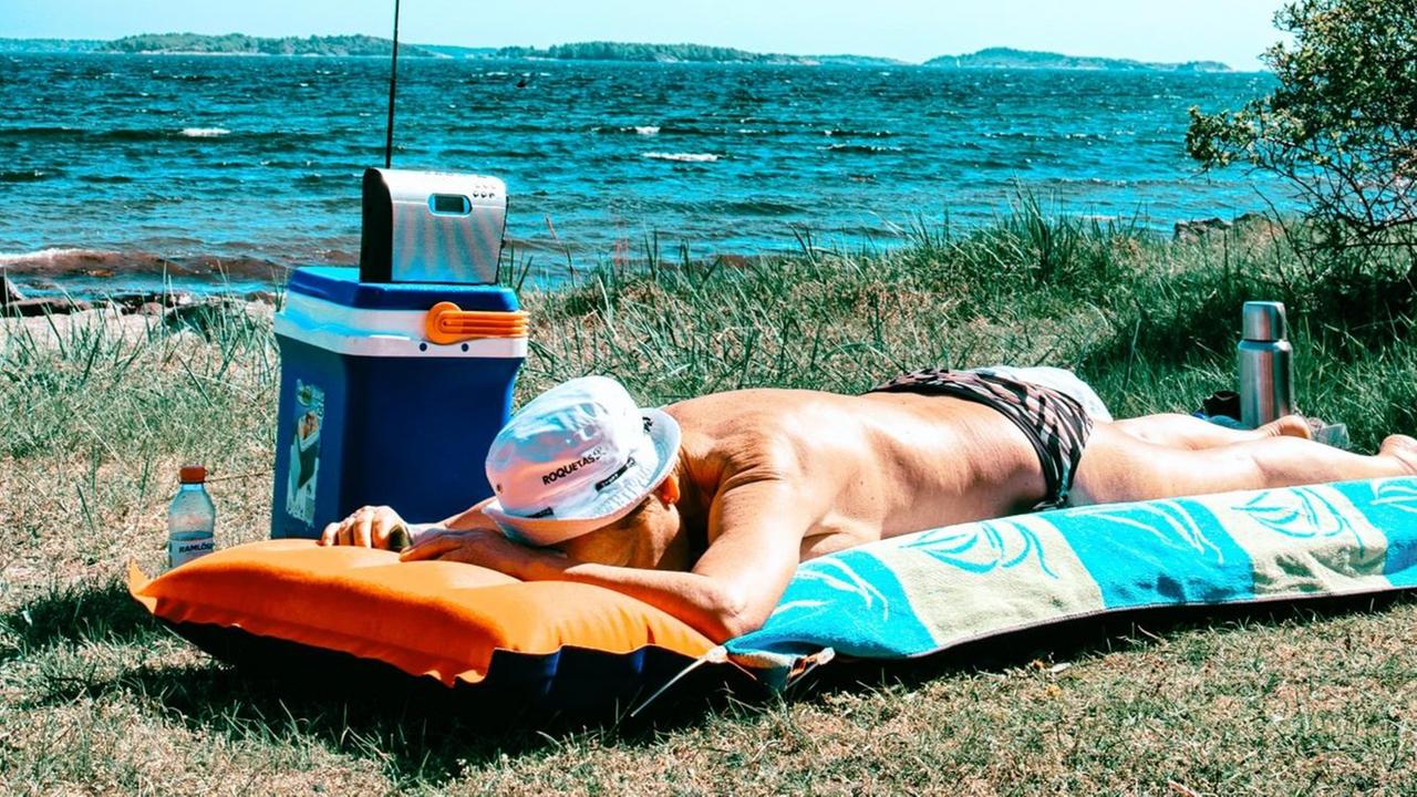 Ein Mann liegt am Wasser auf einer Luftmatratze und hört Radio.