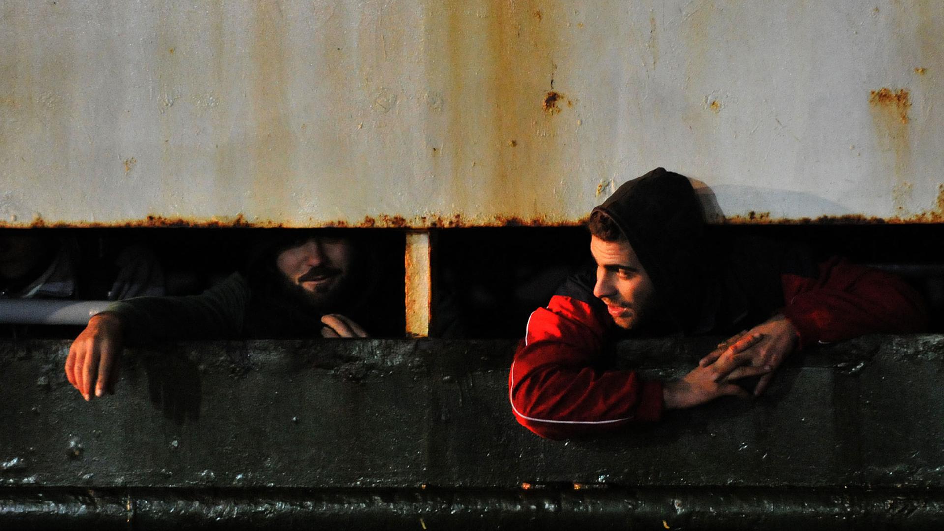 Zwei Flüchtlinge schauen aus einem Fensterschlitz an Bord des führerlos umhertreibenden Frachters "Ezadeen" heraus.
