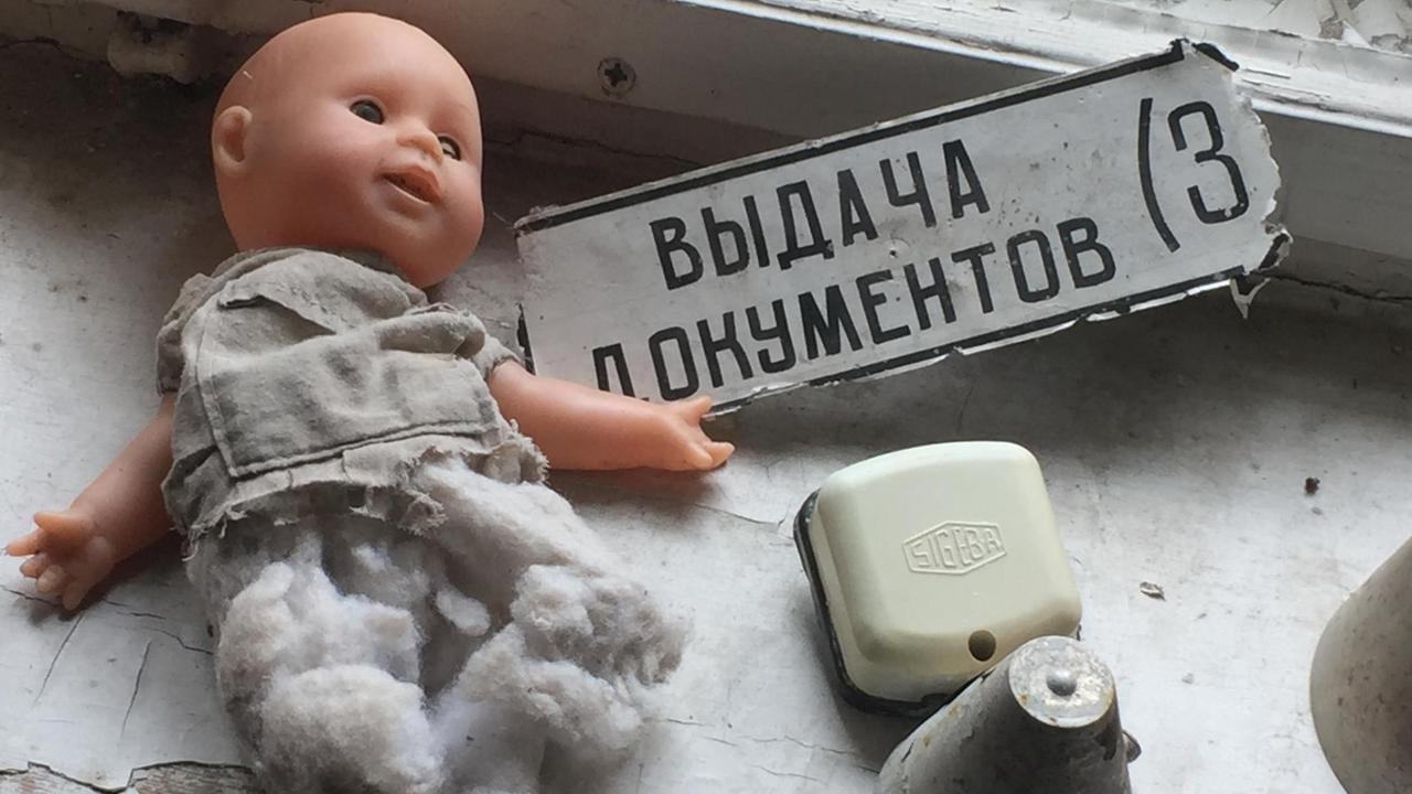 Eine Puppe ohne Beine liegt neben einem Schild mit kyrillischer Schrift auf einem Fensterbrett.