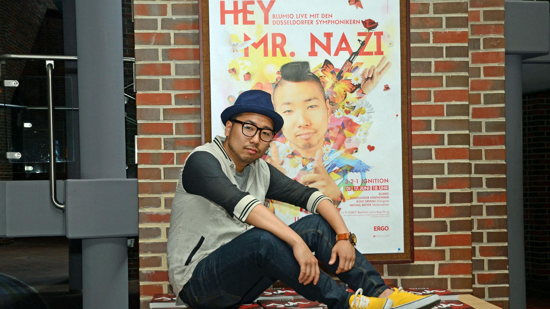 Blumio, der deutsche Rapper japanischer Abstammung, posiert am 12.06.2014 vor einem Plakat mit dem Titel «Hey Mr. Nazi» in der Tonhalle in Düsseldorf (Nordrhein-Westfalen). Der Rapper, der mit bürgerlichem Namen Fumio Kuniyoshi heißt, wird am 17. Juni 2014 gemeinsam mit den Düsseldorfer Symphonikernlive in der Tonhalle auftreten. Blumio, der deutsche Rapper japanischer Abstammung, posiert am 12.06.2014 vor einem Plakat mit dem Titel «Hey Mr. Nazi» in der Tonhalle in Düsseldorf (Nordrhein-Westfalen). Der Rapper, der mit bürgerlichem Namen Fumio Kuniyoshi heißt, wird am 17. Juni 2014 gemeinsam mit den Düsseldorfer Symphonikernlive in der Tonhalle auftreten.
