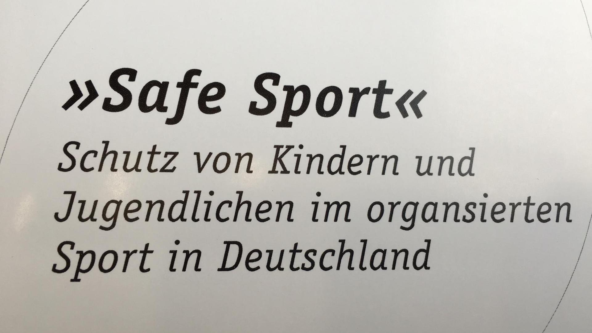 Ein weißes Schild mit der Aufschrift "Safe Sport" - Schutz von Kindern und Jugendlichen im organisierten Sport in Deutschland