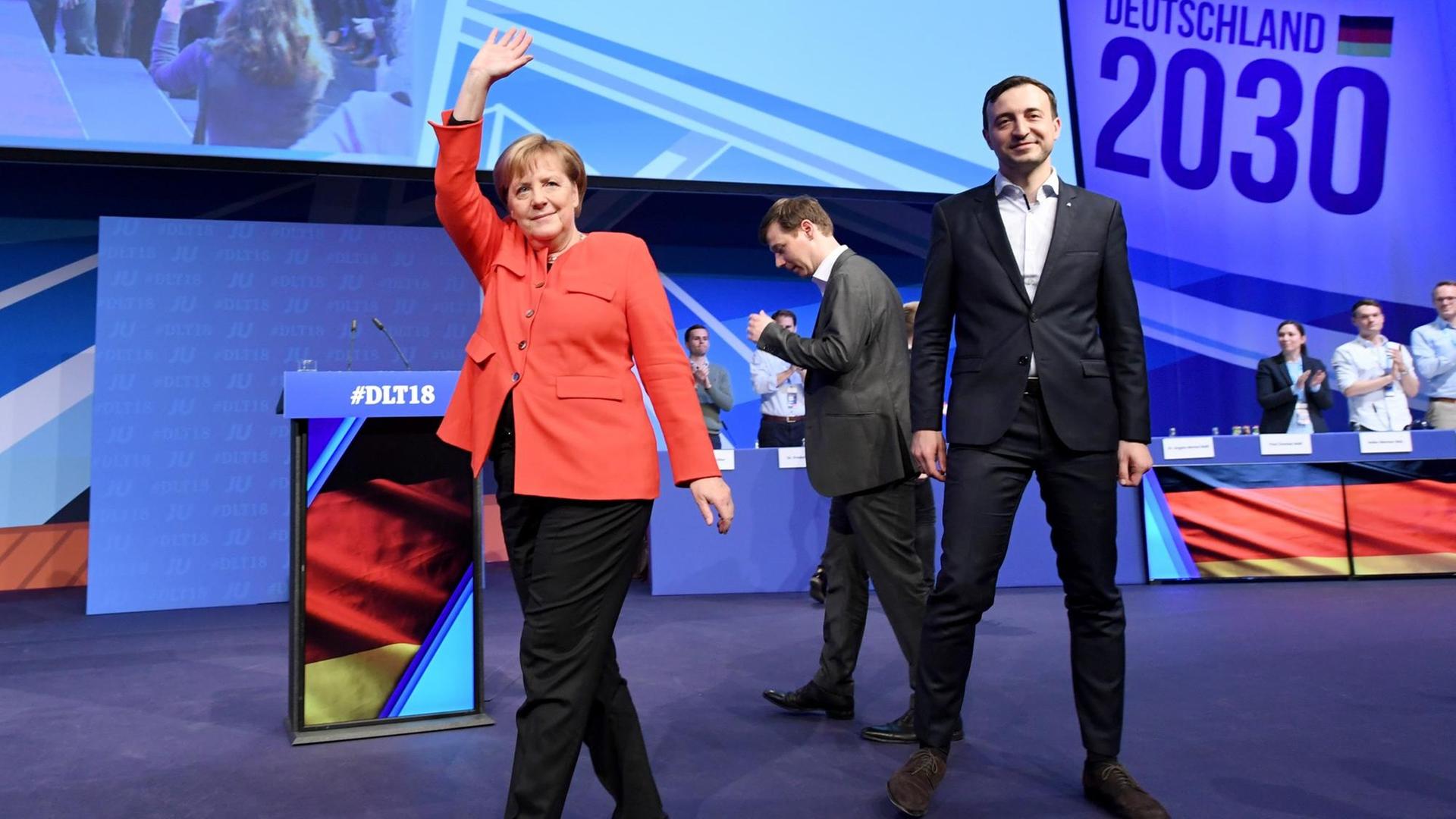 Merkel geht über die Bühne und hebt winkend den rechten Arm. Neben ihr Tobias Loose, Landesvorsitzender JU Schleswig-Holstein, und Paul Ziemiak, Bundesvorsitzender der Jungen Union Deutschland (JU). Merkel geht über die Bühne und hebt winkend den rechten Arm. Neben ihr Tobias Loose, Landesvorsitzender JU Schleswig-Holstein, und Paul Ziemiak, Bundesvorsitzender der Jungen Union Deutschland (JU).