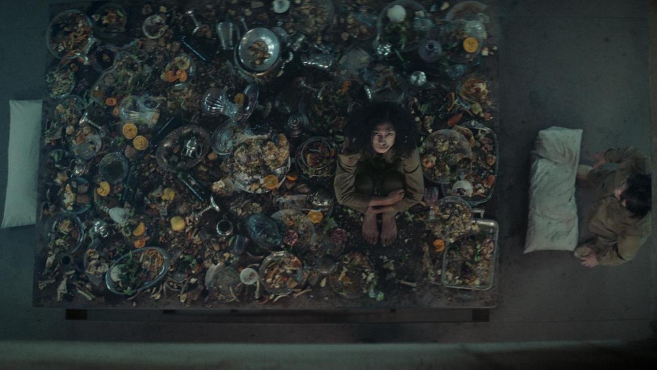 Szene aus dem Thriller "Der Schacht": Ein Mädchen sitzt auf einem Tisch voller Essenreste Szene aus dem Thriller "Der Schacht": Ein Mädchen sitzt auf einem Tisch voller Essenreste