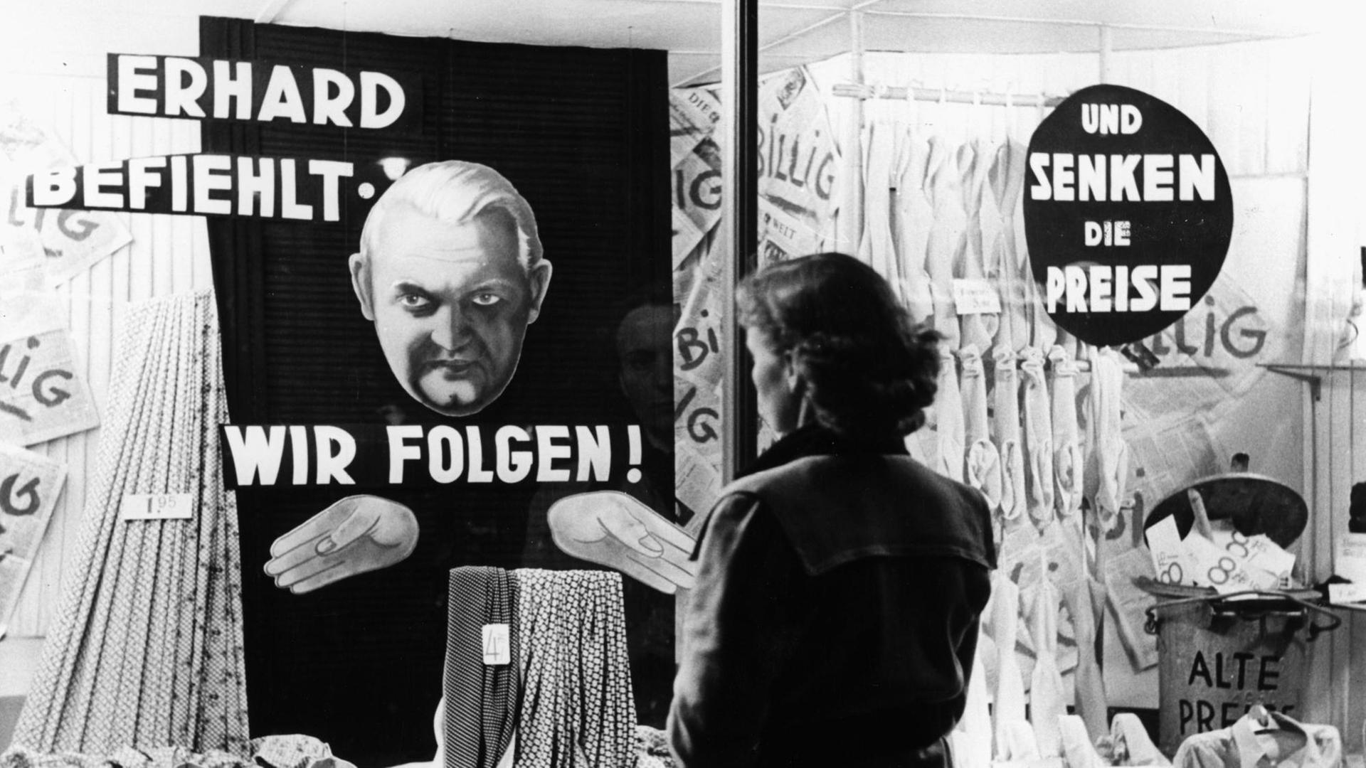 Eine Frau steht vor einem Schaufenster. In dem Schaufenster steht "Erhard befiehlt - wir folgen! und senken die Preise". Das Foto ist von circa 1949/50. Eine Frau steht vor einem Schaufenster. In dem Schaufenster steht "Erhard befiehlt - wir folgen! und senken die Preise". Das Foto ist von circa 1949/50.