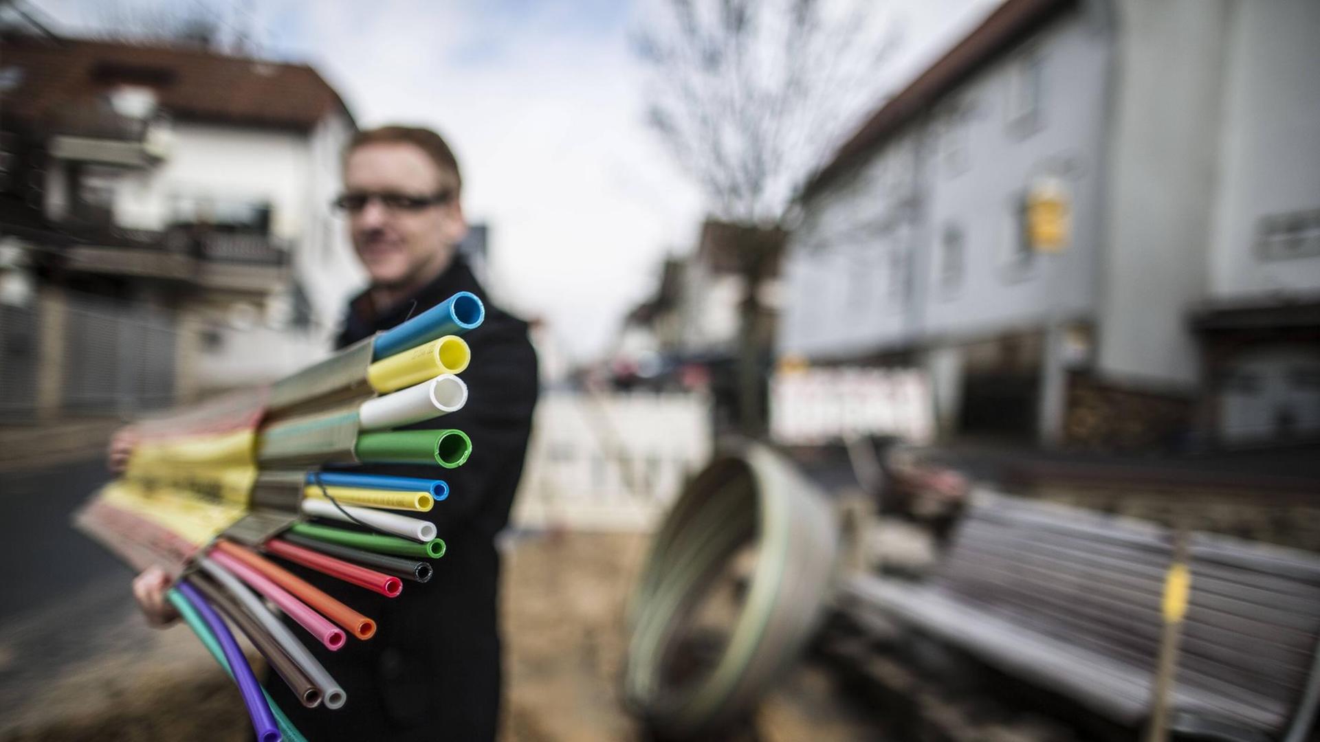 Ein Mann hält vor einer aufgerissenen Straße Leerrohre für den Breitband-Ausbau in die Kamera. Ein Mann hält vor einer aufgerissenen Straße Leerrohre für den Breitband-Ausbau in die Kamera.