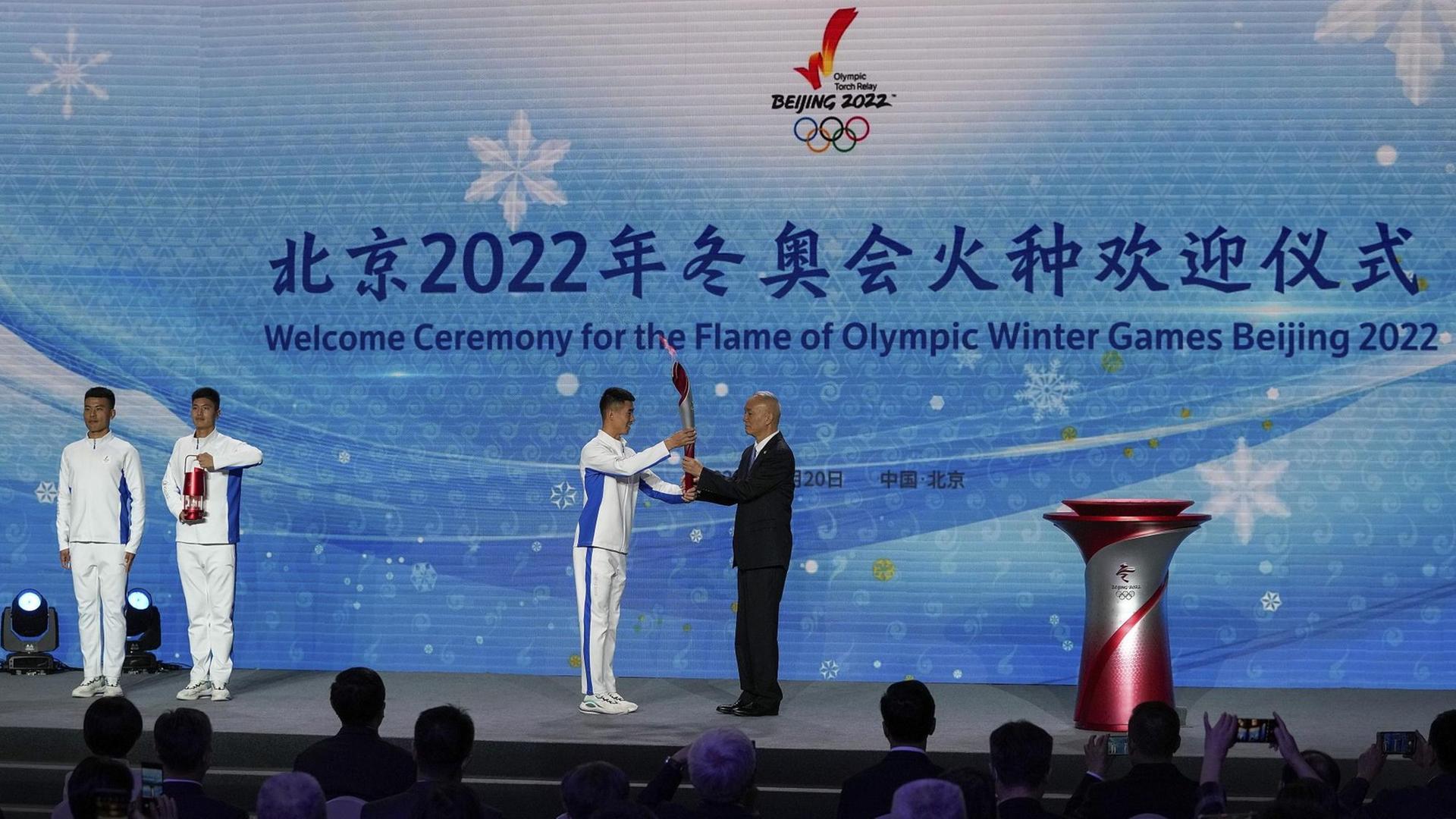 Peking: Ein Sportler übergibt die olympische Fackel an Cai Qi, Sekretär der Kommunistischen Partei Pekings, während der Begrüßungszeremonie zur Ankunft der olympischen Flamme für die Olympischen Winterspiele Peking 2022 im Olympiaturm.