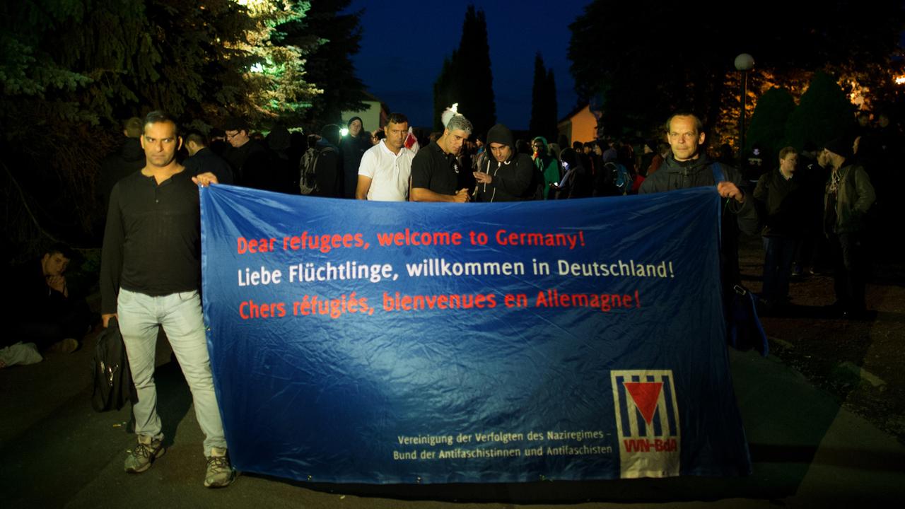 Zwei Männer halten am 23.06.2015 einen Banner "Dear refugees, welcome to Germany! Liebe Flüchtlinge, willkommen in Deutschland! Chers refugies, bienvenues em Allemagne!" vor eine Unterbringung von Asylbewerbern (Leonardo-Hotel) in Freital (Sachsen) in den Händen.