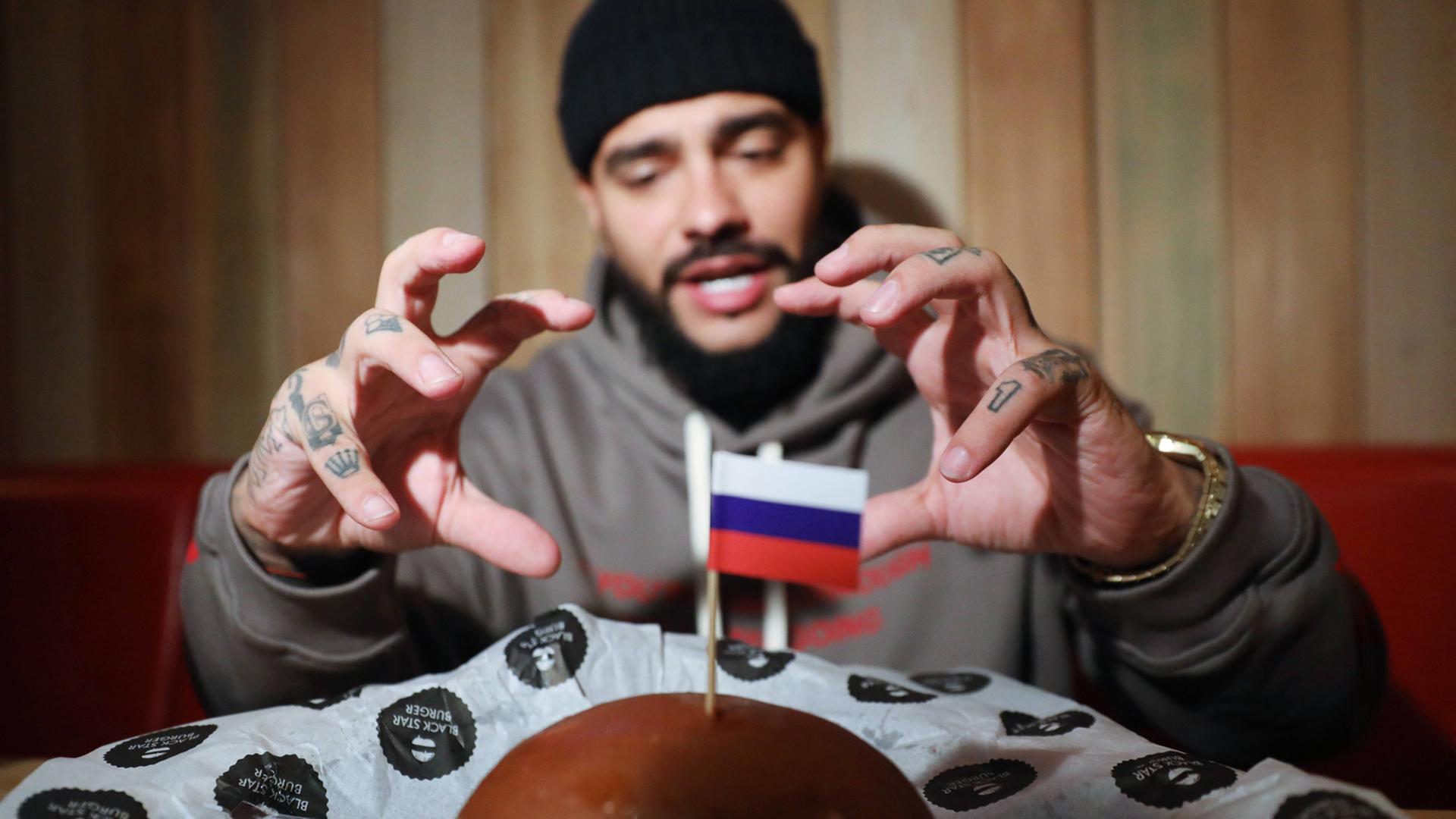 Der Hip-Hop-Sänger Timati verkauft auf seinem Label nicht nur Musik, sondern auch Burger - hier sieht man ihn, wie er nach einem sogenannten "Präsidenten-Burger" mit kleiner Russland-Flagge greift, den es zum Putin-Geburtstag zum Verkauf gab Der Hip-Hop-Sänger Timati verkauft auf seinem Label nicht nur Musik, sondern auch Burger - hier sieht man ihn, wie er nach einem sogenannten "Präsidenten-Burger" mit kleiner Russland-Flagge greift, den es zum Putin-Geburtstag zum Verkauf gab