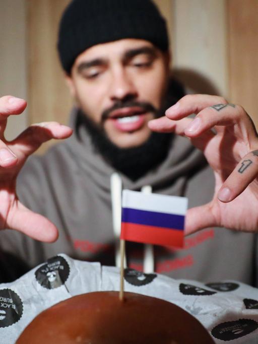 Der Hip-Hop-Sänger Timati verkauft auf seinem Label nicht nur Musik, sondern auch Burger - hier sieht man ihn, wie er nach einem sogenannten "Präsidenten-Burger" mit kleiner Russland-Flagge greift, den es zum Putin-Geburtstag zum Verkauf gab