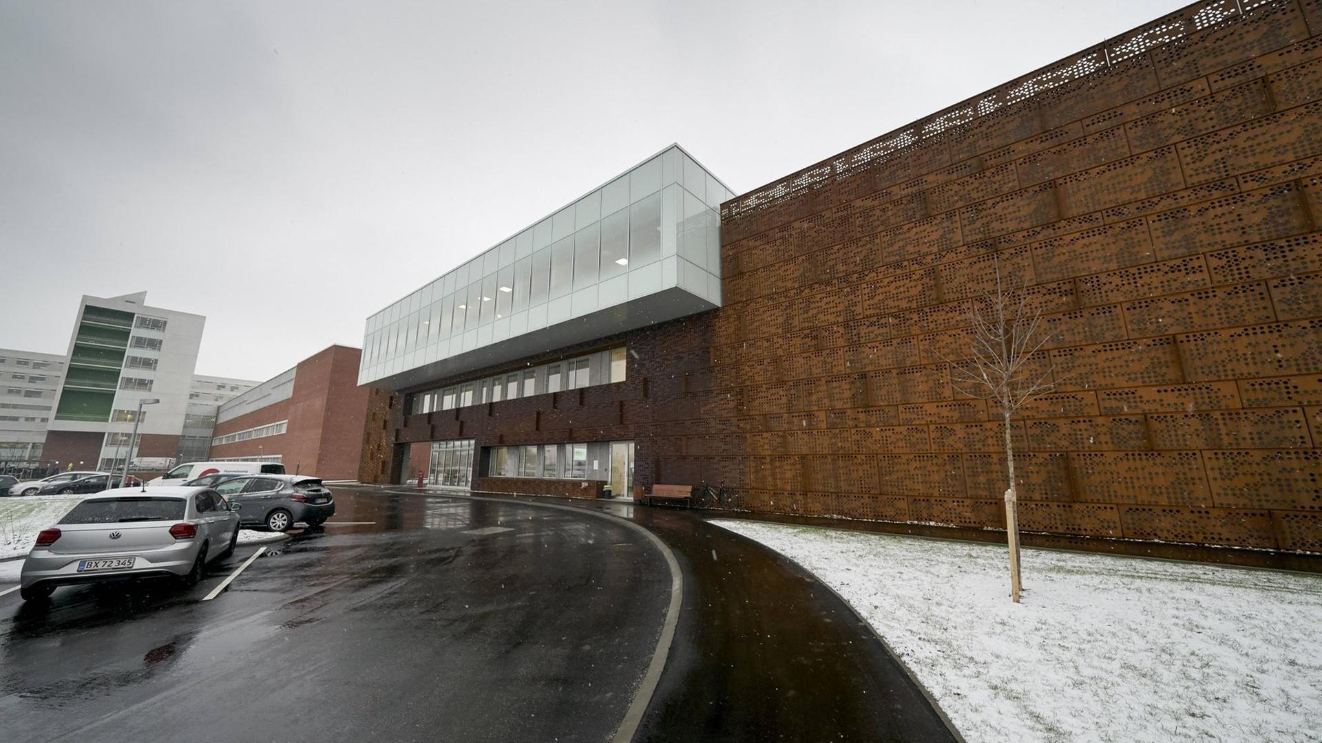 In einer verschneiten Straße ragen die dunklen Mauern des Universitätsklinikum Aarhus auf. In einer verschneiten Straße ragen die dunklen Mauern des Universitätsklinikum Aarhus auf.
