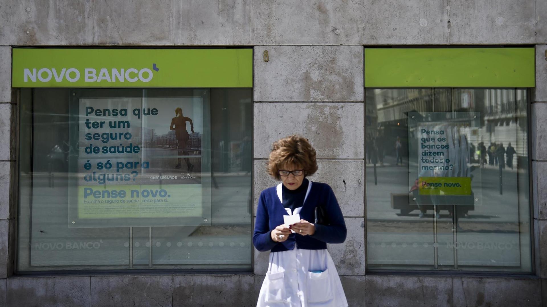 Eine Zweigstelle der Novo Banco in Lissabon am 31. März 2017, mit Werbeslogans im Fenster. Im Vordergrund eine Frau.