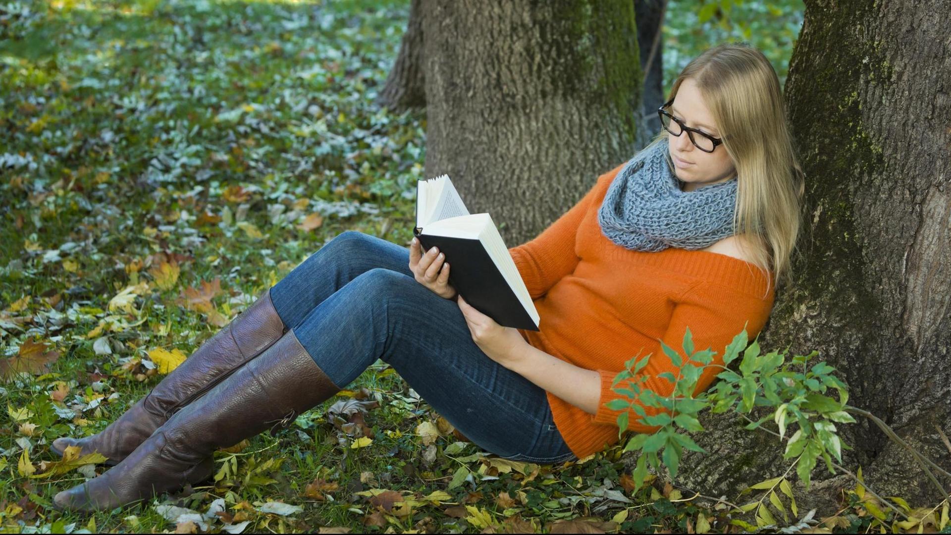 Junge Frau mit Brille sitzt im Park und liest ein Buch. Junge Frau mit Brille sitzt im Park und liest ein Buch.