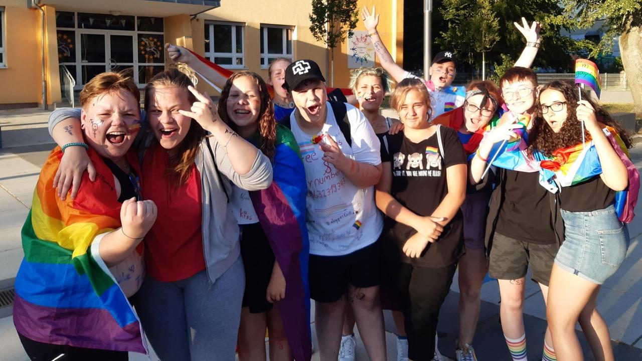 Eine Gruppe junger Menschen mit Regenbogenfahnen vor einer Schule Eine Gruppe junger Menschen mit Regenbogenfahnen vor einer Schule