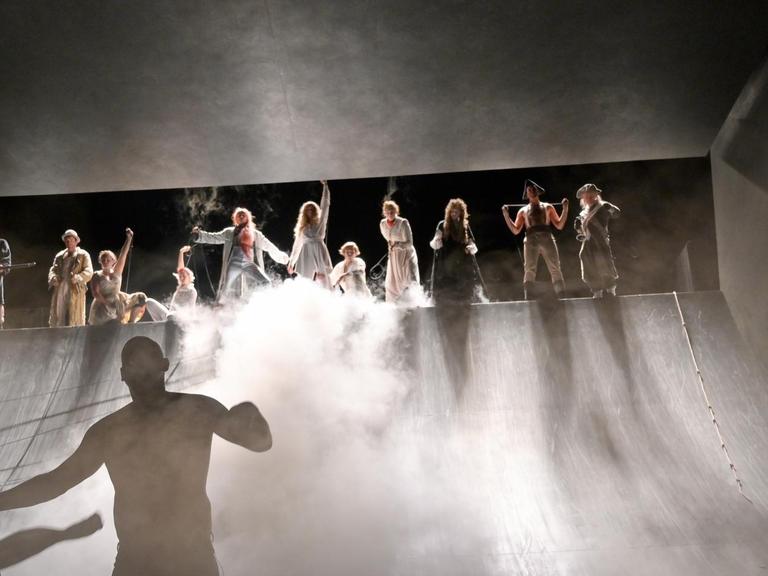 Das Bühnenbild im Düsseldorfer von "Dantons Tod" zeigt eine mit Nebenschwaden durchzogene Szenerie, in der sich zwei Seiten von Menschengruppen zeigen.
