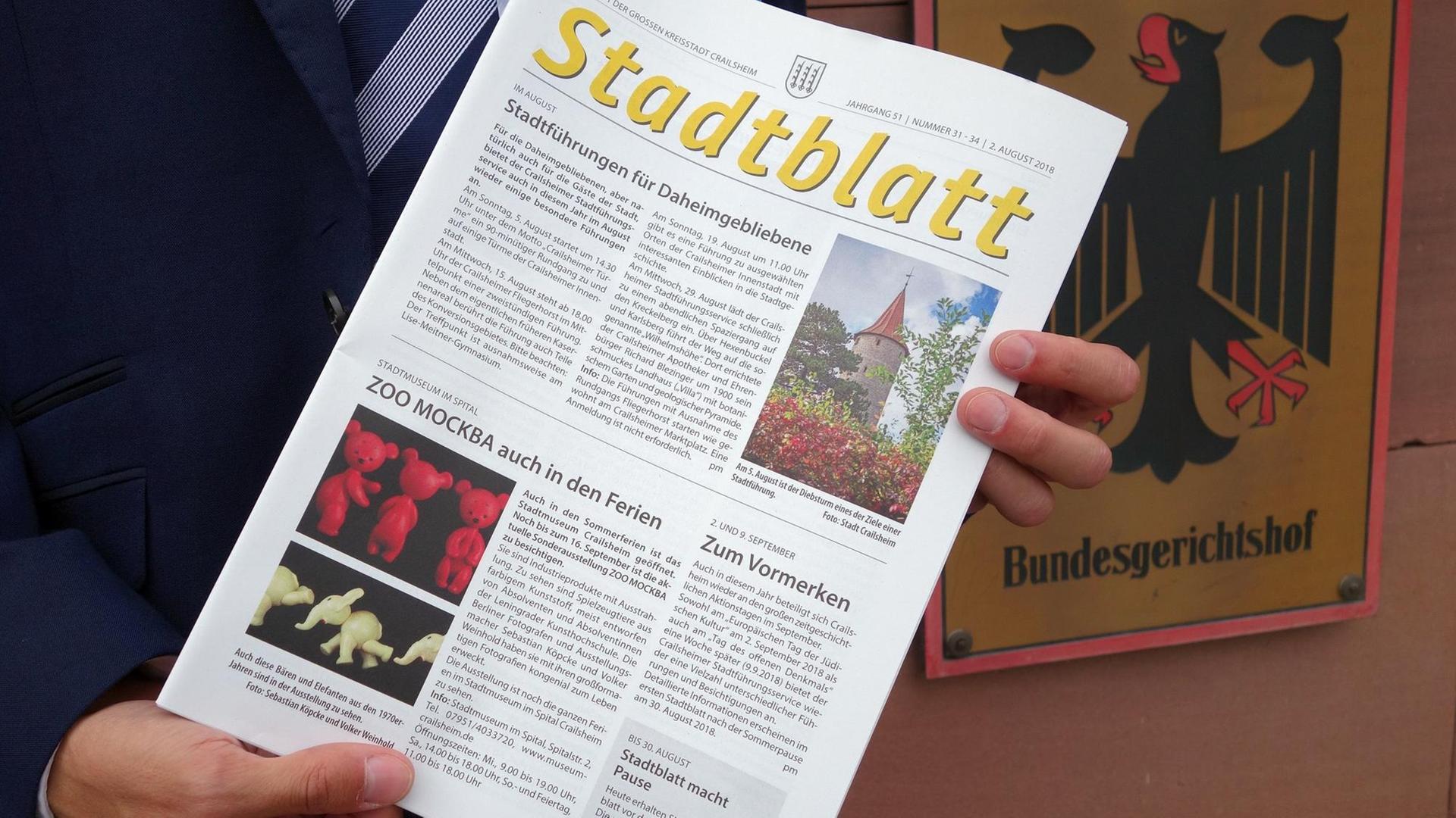 Eine Ausgabe des Amtsblattes der Stadt Crailsheim wird von zwei Händen gehalten. Dahinter das Schild des Bundesgerichtshofes. Eine Ausgabe des Amtsblattes der Stadt Crailsheim wird von zwei Händen gehalten. Dahinter das Schild des Bundesgerichtshofes.