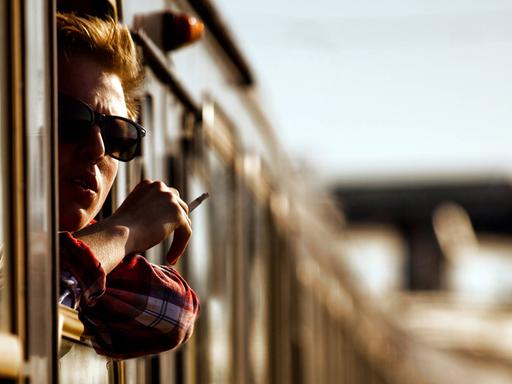 Ein junger Mann mit Zigarette schaut aus einem Zugfenster