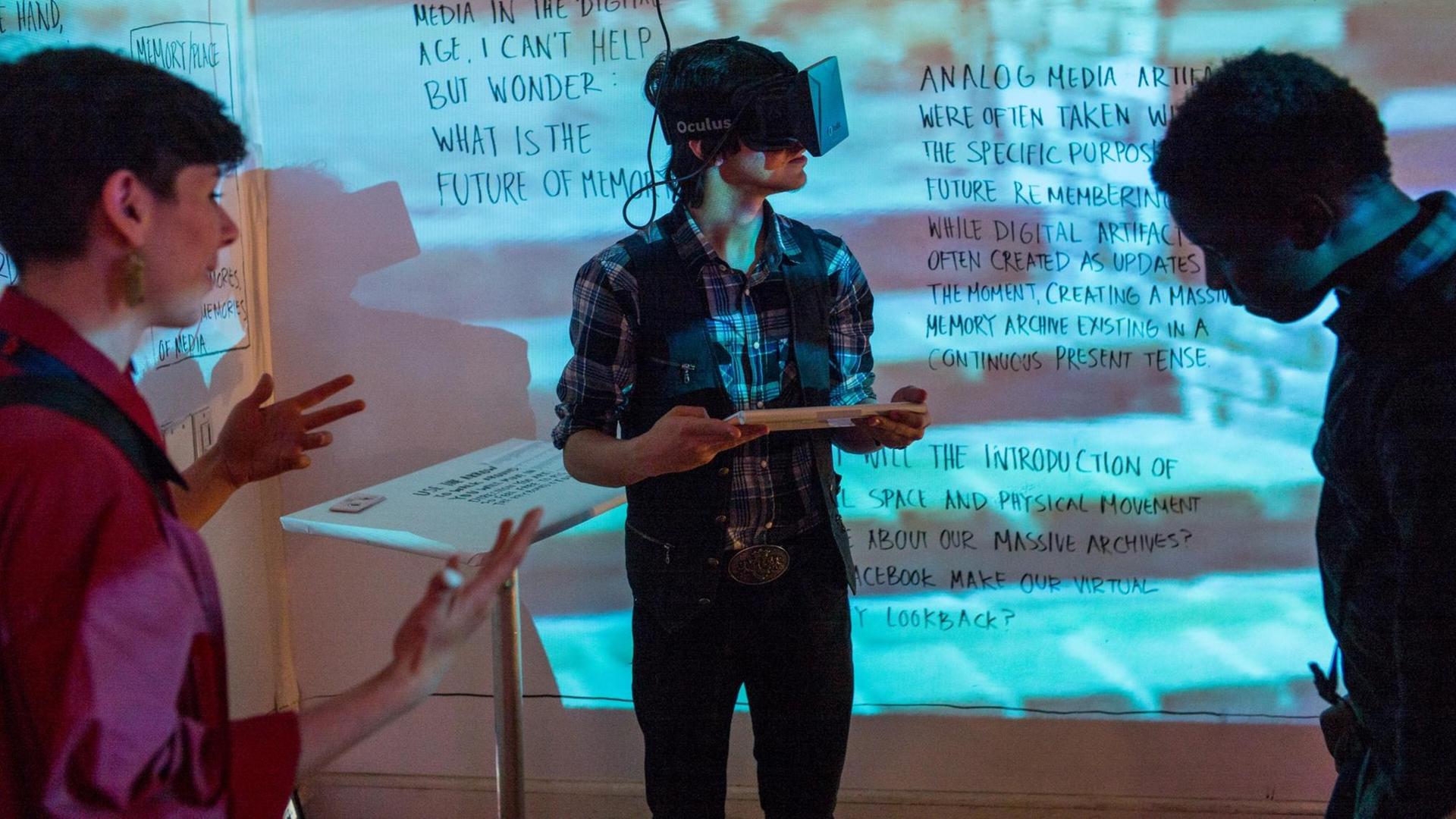 Eine Mann mit VR-Brille vor einem Whiteboard. Zwei andere Menschen beobachten ihn. Eine Mann mit VR-Brille vor einem Whiteboard. Zwei andere Menschen beobachten ihn.