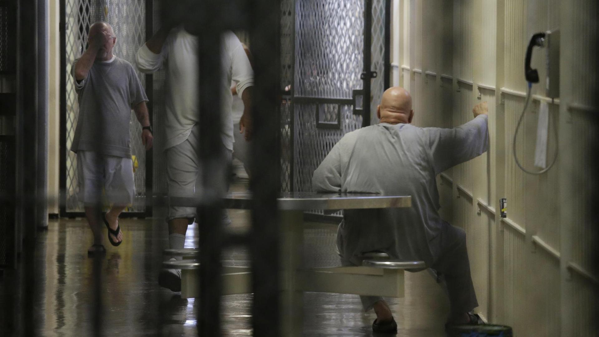 Blick in den Todestrakt durch Gitterstäbe im Vordergrund. Im Gang sind Insassen zu sehen.