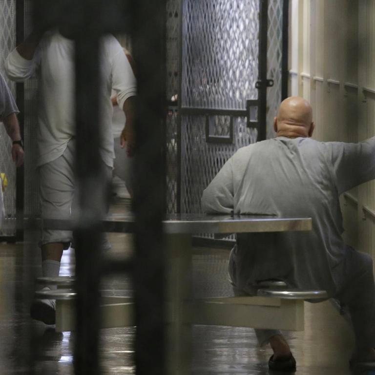 Blick in den Todestrakt durch Gitterstäbe im Vordergrund. Im Gang sind Insassen zu sehen.