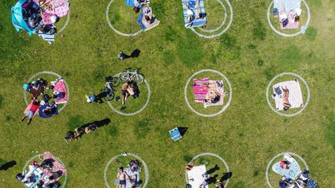 Menschen liegen in einem Park in vorgezeichneten Kreisen um den nötigen Abstand einzuhalten.