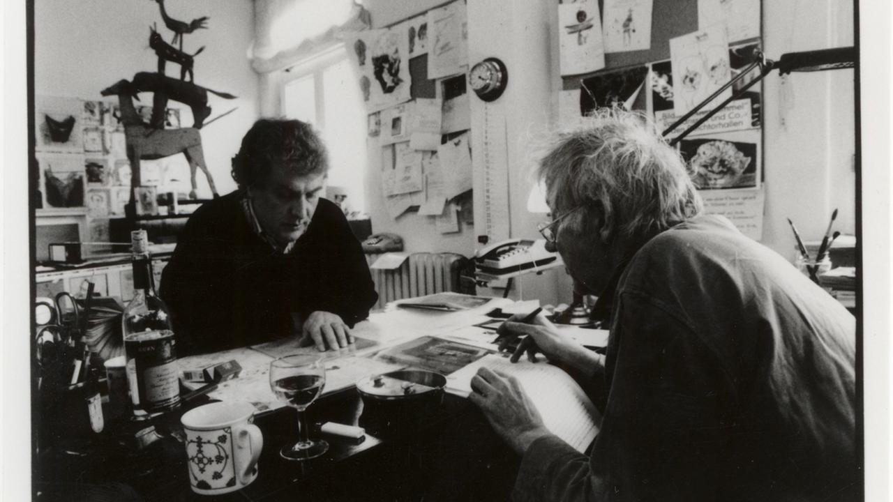 Ein schwarz weisses Bild auf dem Horst Janssen an einem Tisch mit einem Stift in der Hand sitzt. Er und skizziert und schreibt einen Text.
