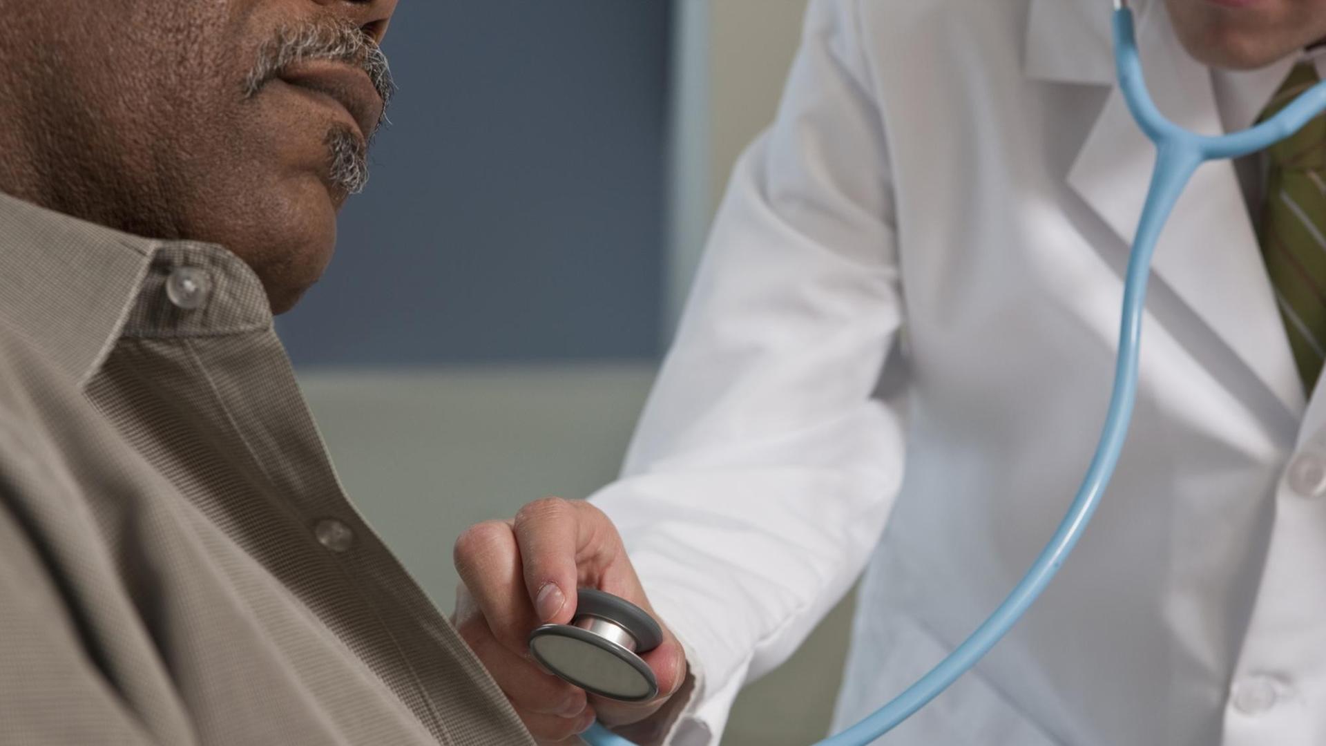Ein Arzt hört die Brust eines Mannes mit einem Stethoskop ab.