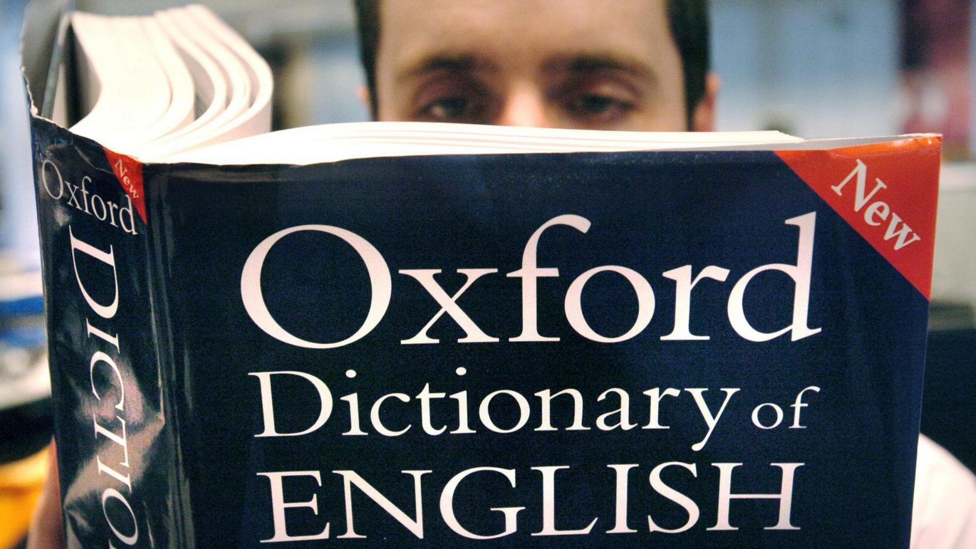 Ein Mann hält ein aufgeschlagenes Exemplar des "Oxford Dictionary of English"; die weiße Schrift steht auf dunkelblauem Grund.