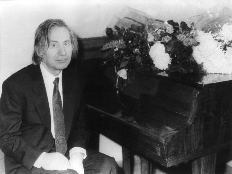 Der russische Komponist und Pianist Alfred Schnittke, schwarz-weiß-Aufnahme, an einem Klavier sitzend, in die Kamera blickend.