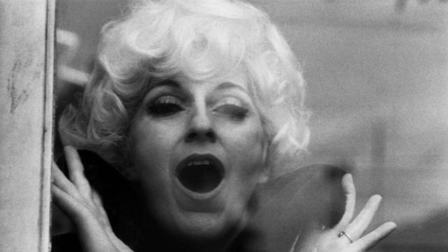 Schwarz-Weiß Foto mit dem Kopf der blond gelockten Sängerin Cathy Berberian: Sie singt mit weit geöffnetem Mund, ihre Hände sind gespreizt.