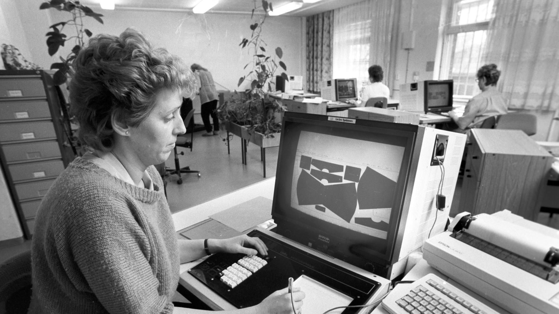 Eine Frau bei der Arbeit an einem Computer zur Optimierung des Zuschnitts von Bekleidungsteilen aus den Stoffen, aufgenommen im VEB Wäschekonfektion Lößnitz im April 1989. Eine Frau bei der Arbeit an einem Computer zur Optimierung des Zuschnitts von Bekleidungsteilen aus den Stoffen, aufgenommen im VEB Wäschekonfektion Lößnitz im April 1989.