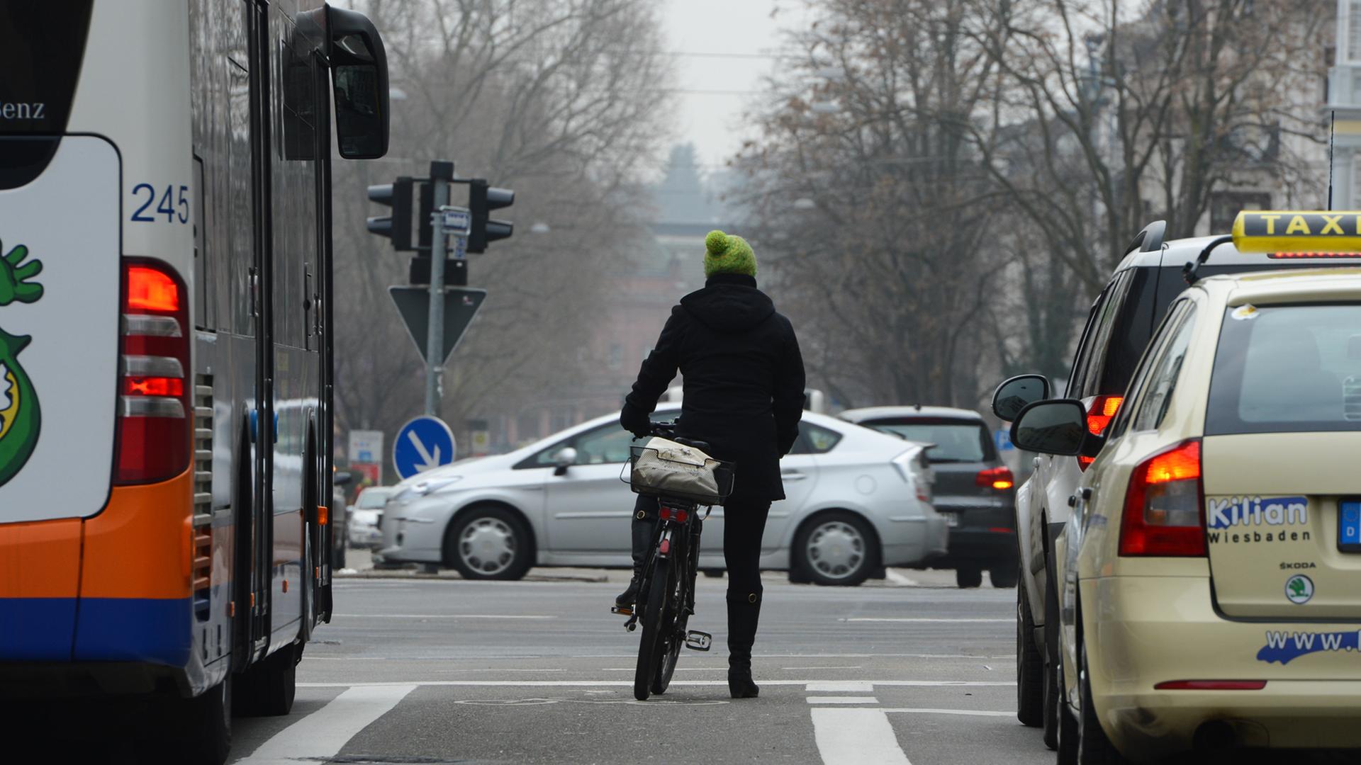 Eine Frau steht am 18.02.2015 in Wiesbaden (Hessen) mit ihrem Fahrrad an einer belebten Kreuzung. Eine Frau steht am 18.02.2015 in Wiesbaden (Hessen) mit ihrem Fahrrad an einer belebten Kreuzung.