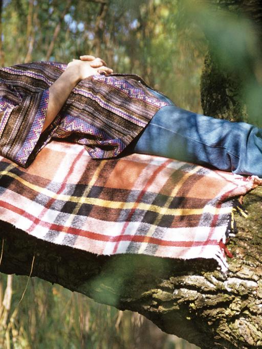 Ein Mann liegt schlafend auf einem Ast eines Baumes.
