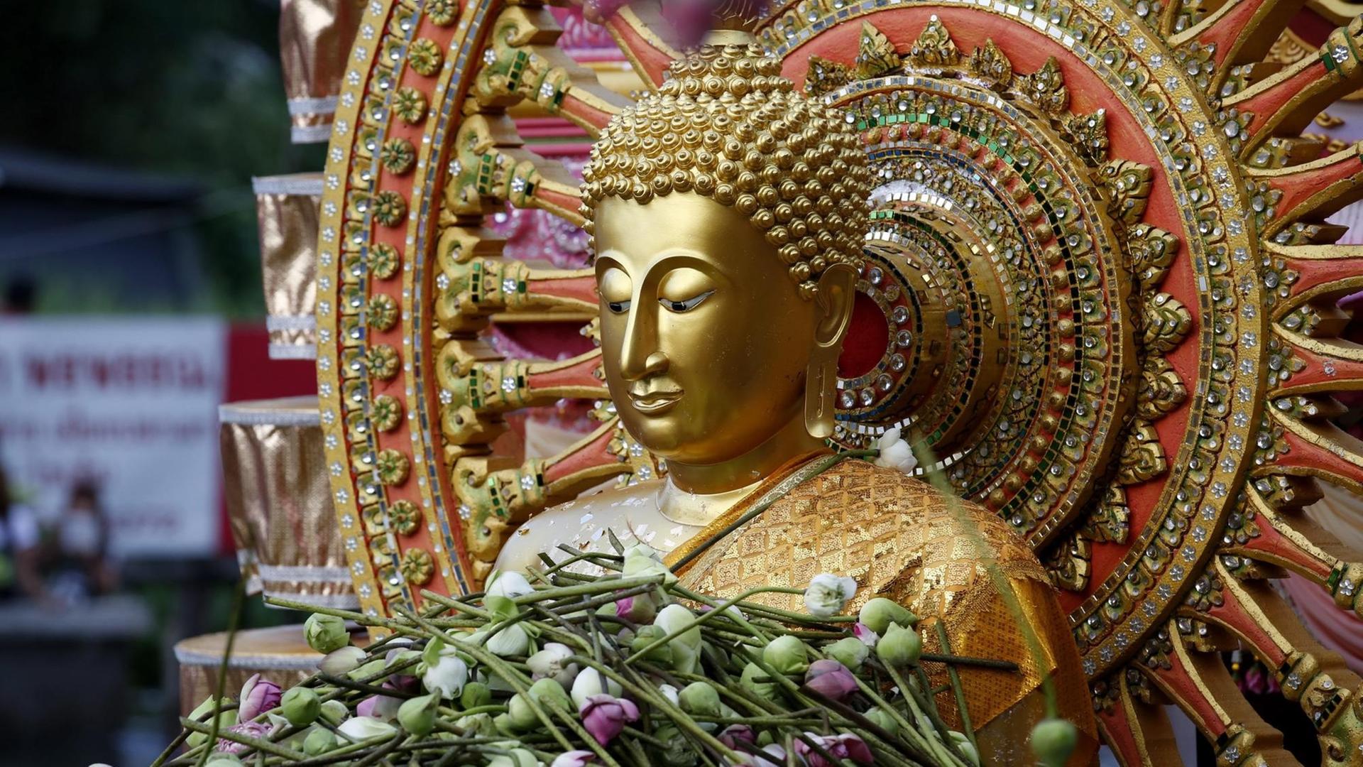Ein Buddha in Bangkok, der im Rahmen einer religiösen Zeremonie mit Lotusblumen überhäuft ist