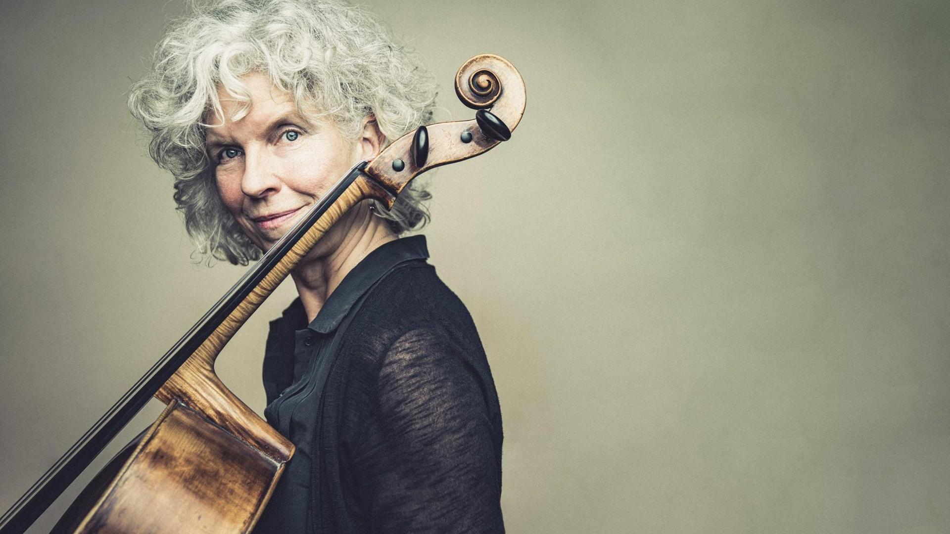 Eine grauhaarige Frau schaut hinter einem an ihren Körper angelehnten Cello seitlich nach vorne Eine grauhaarige Frau schaut hinter einem an ihren Körper angelehnten Cello seitlich nach vorne
