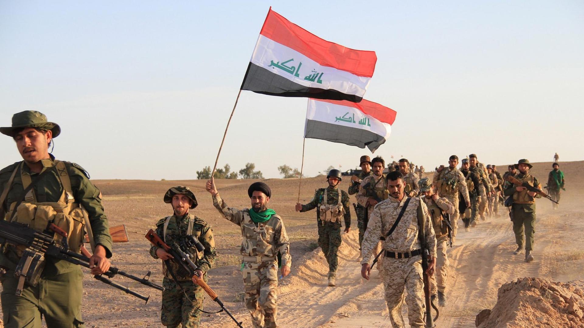 Irakische Soldaten und Mitgliedern privater Milizen, die auf Regierungsseite kämpfen, tragen am 31. März 2015 in Tikrit die Flagge des Irak während eines Kampfes gegen den sogenannten "Islamischen Staat" . Auf der Flagge ist der arabischen Ausdruck "Allahu Akbar" zu lesen.