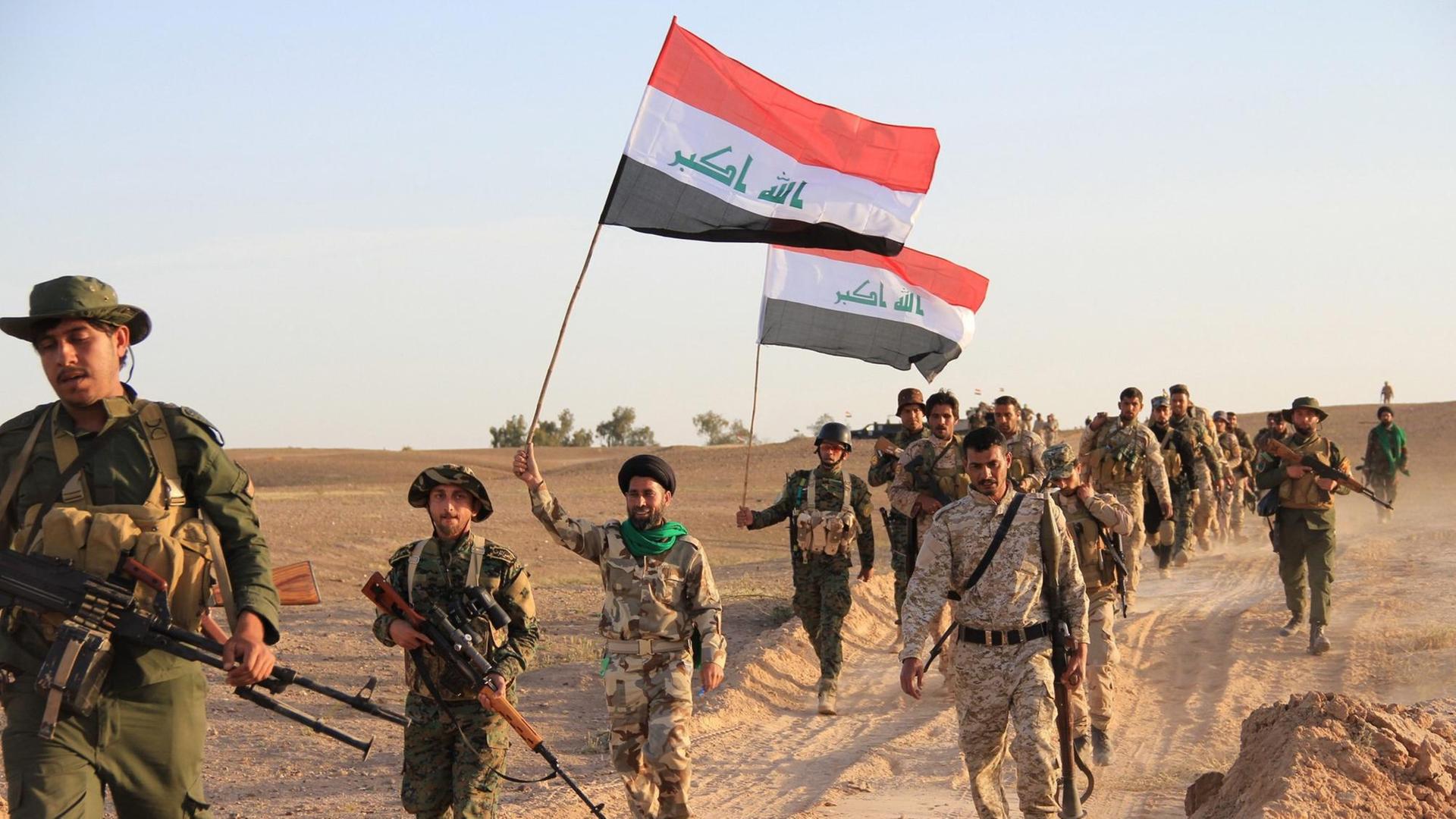 Irakische Soldaten und Mitgliedern privater Milizen, die auf Regierungsseite kämpfen, tragen am 31. März 2015 in Tikrit die Flagge des Irak während eines Kampfes gegen den sogenannten "Islamischen Staat" . Auf der Flagge ist der arabischen Ausdruck "Allahu Akbar" zu lesen. Irakische Soldaten und Mitgliedern privater Milizen, die auf Regierungsseite kämpfen, tragen am 31. März 2015 in Tikrit die Flagge des Irak während eines Kampfes gegen den sogenannten "Islamischen Staat" . Auf der Flagge ist der arabischen Ausdruck "Allahu Akbar" zu lesen.