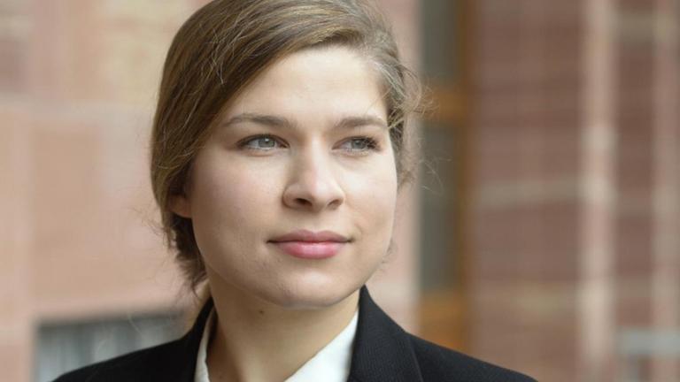 Die Autorin Nele Pollatschek steht in dunkelblauer Bluse und schwarzem Blazer vor einer rötlichen Wand Die Autorin Nele Pollatschek steht in dunkelblauer Bluse und schwarzem Blazer vor einer rötlichen Wand