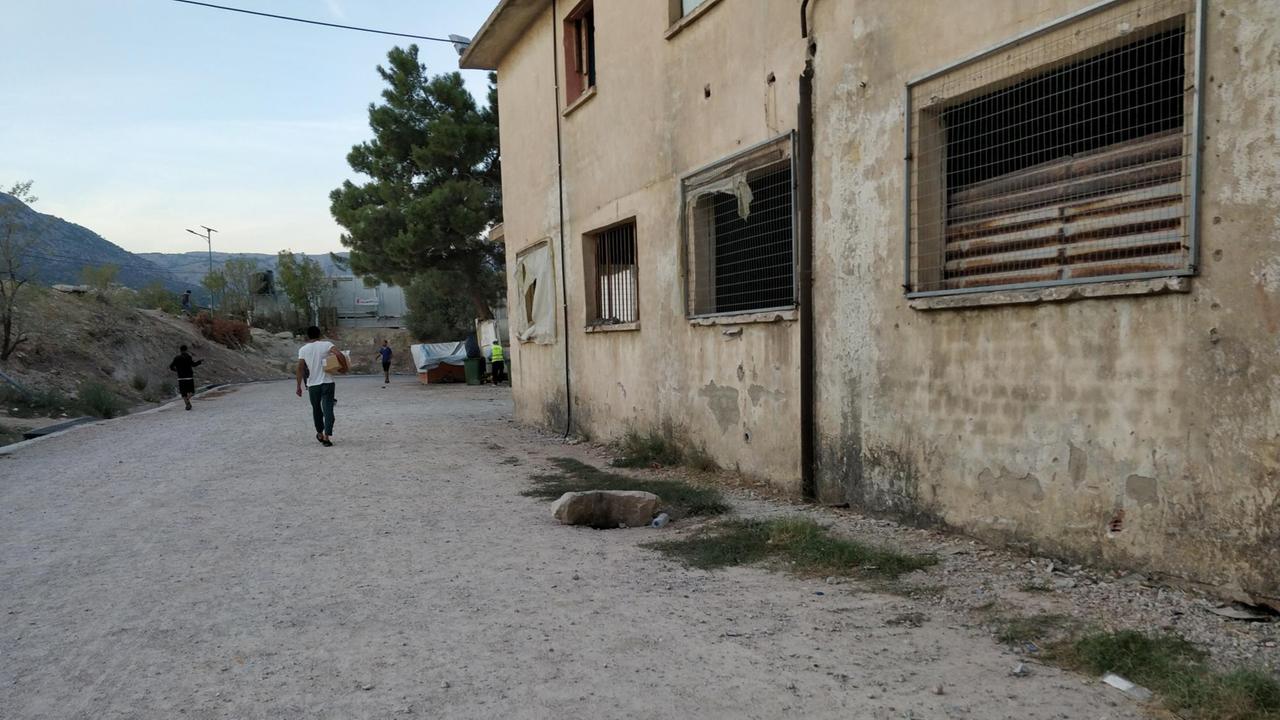 Männer gehen an einem heruntergekommenen Flüchtlingsheim vorbei.