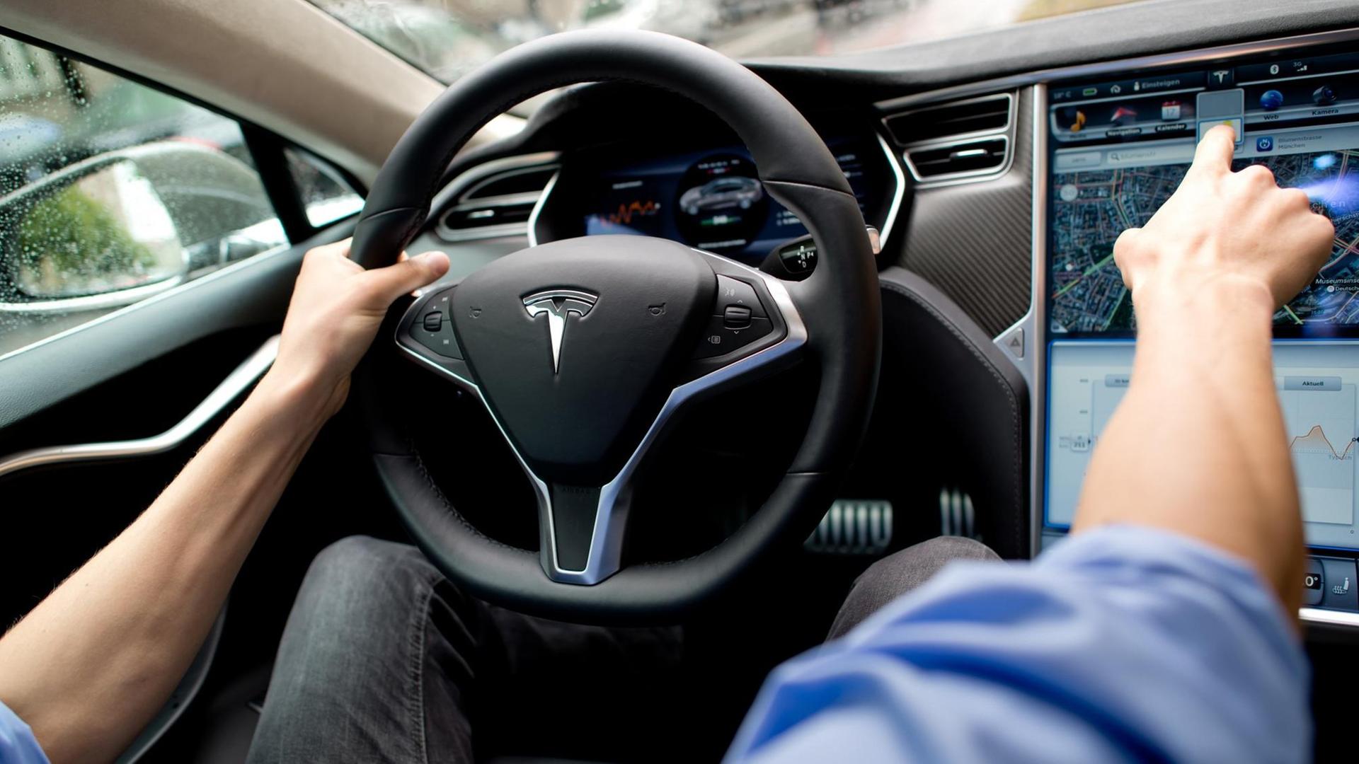 Ein Mann sitzt in einem Tesla Model S auf dem Fahrersitz vor einem Showroom des Autoherstellers. Ein Mann sitzt in einem Tesla Model S auf dem Fahrersitz vor einem Showroom des Autoherstellers.